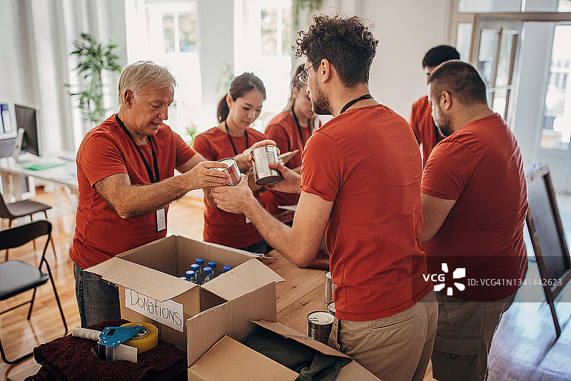 志愿者团队在捐赠中心分享和包装食物、衣服和水，用盒子装好送给有需要的人图片素材