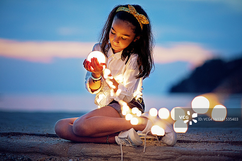 小女孩坐在码头上玩神秘的灯光图片素材