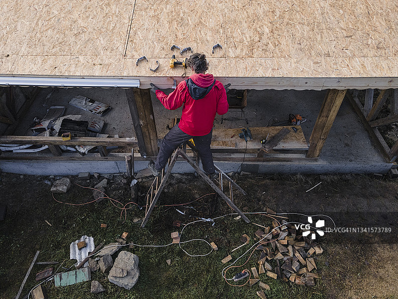 DIY家居改善：男子修理谷仓屋顶的鸟瞰图图片素材