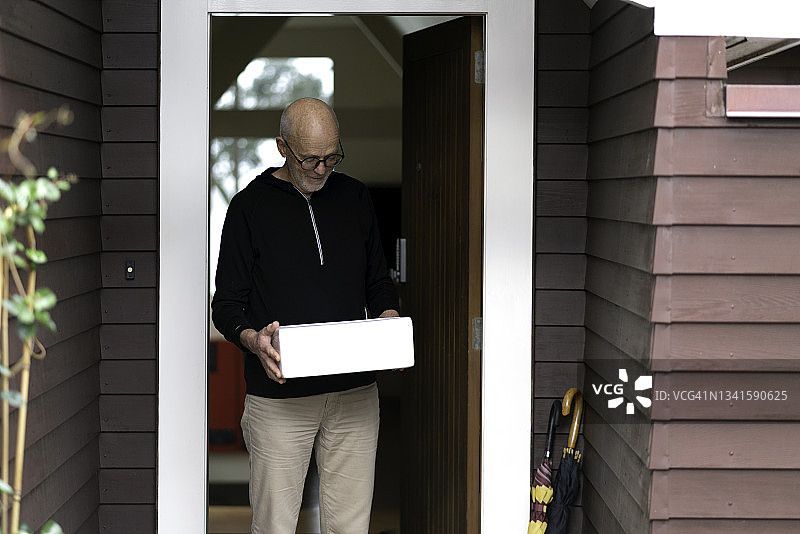 年长的男人在他家门口拿起一箱冷藏鱼图片素材