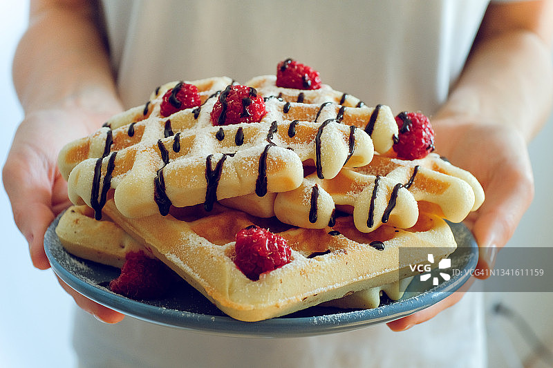 女人或女孩手拿一盘新鲜出炉的华夫饼：烹饪自制食物的概念，爱好，最喜欢的活动，素食和纯素食，美味的浆果甜点图片素材