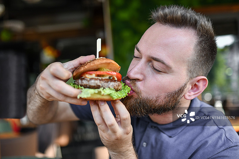 饥饿的男人正在吃美味的汉堡图片素材