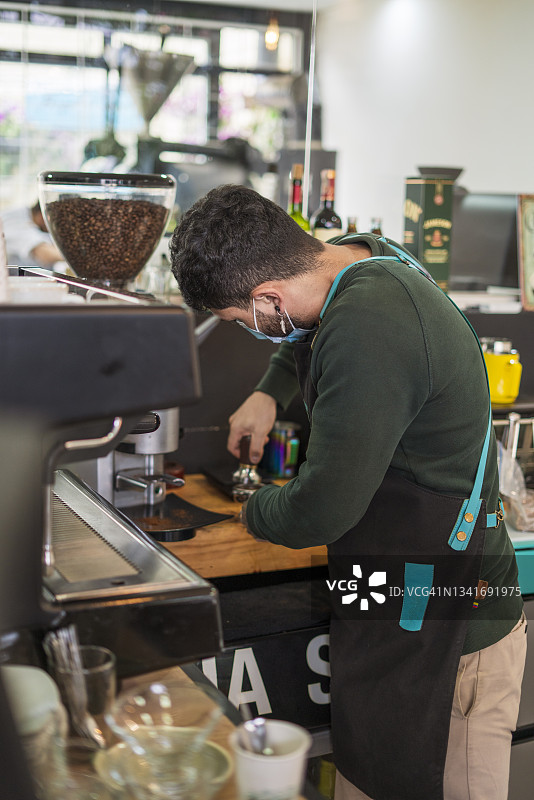 咖啡工厂的拉丁裔男员工站在酒吧里，为顾客准备咖啡。图片素材