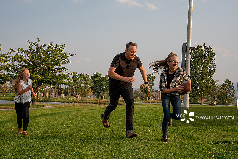 年轻父亲和女儿在公园草地上玩橄榄球图片素材