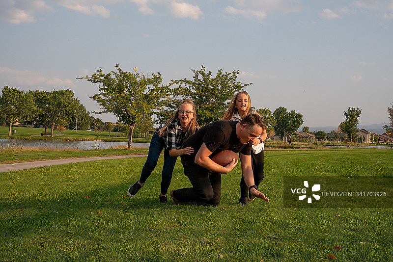 年轻父亲和女儿在公园草地上玩橄榄球图片素材