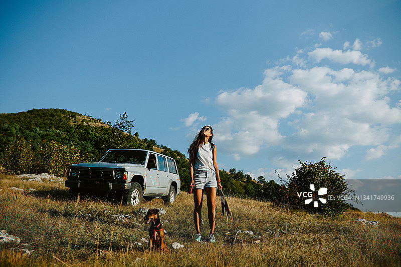 与宠物狗在美丽大自然中自驾游的年轻女人图片素材
