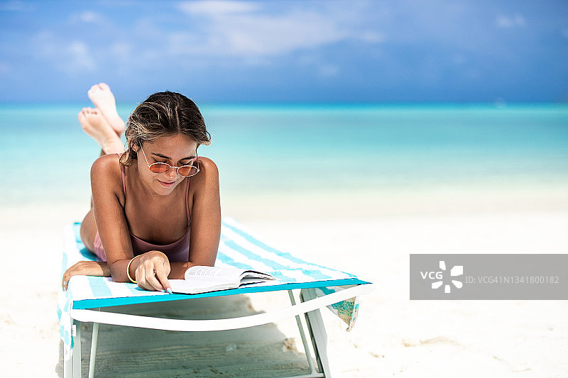 在沙滩躺椅上看书的休闲女人图片素材