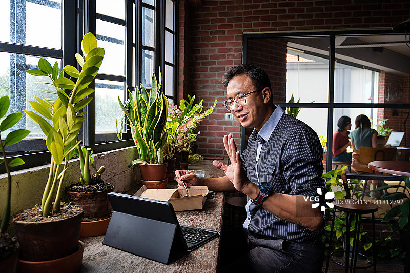 亚洲老年男子在环保自助餐厅午休时享用外卖食物，餐厅里装饰着漂亮的盆栽植物图片素材