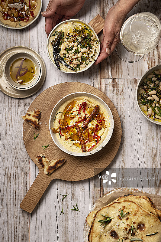鹰嘴豆泥和白腰豆蘸酱，配香料，木桌上有人手捧碗图片素材