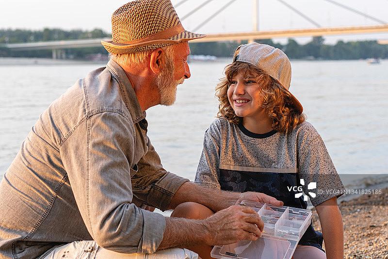 好奇的孙子与祖父和渔夫在河边度过一天，学习有关钓鱼饵料的知识图片素材