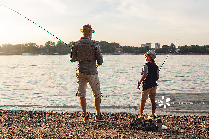 年长的渔夫和孙子在河边享受日落时分一起钓鱼的乐趣图片素材