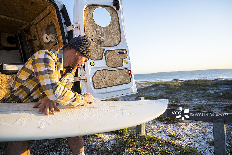 快乐男子在露营车后给冲浪板打蜡特写镜头图片素材