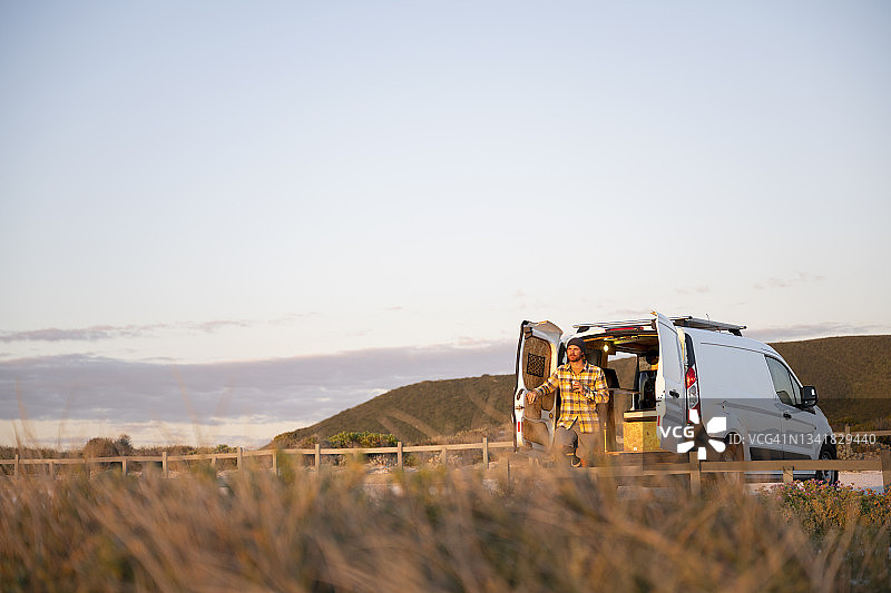 站在露营车后方的男人，前景是长满草的海滩的广角镜头图片素材