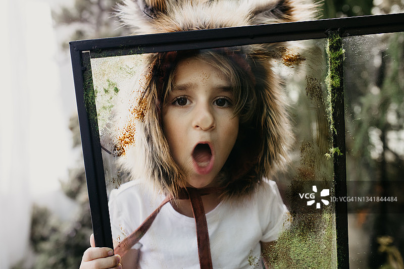 男孩戴着狐狸帽子在温室的窗户上做鬼脸图片素材