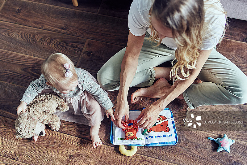 保姆和1岁女童在家里的地板上阅读儿童绘本图片素材