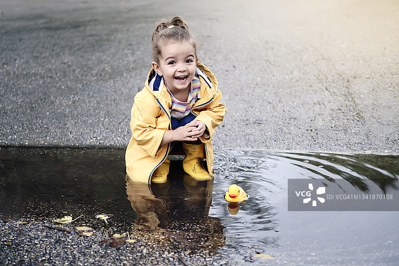 一个3岁的小女孩蹲在水坑里玩橡皮鸭图片素材