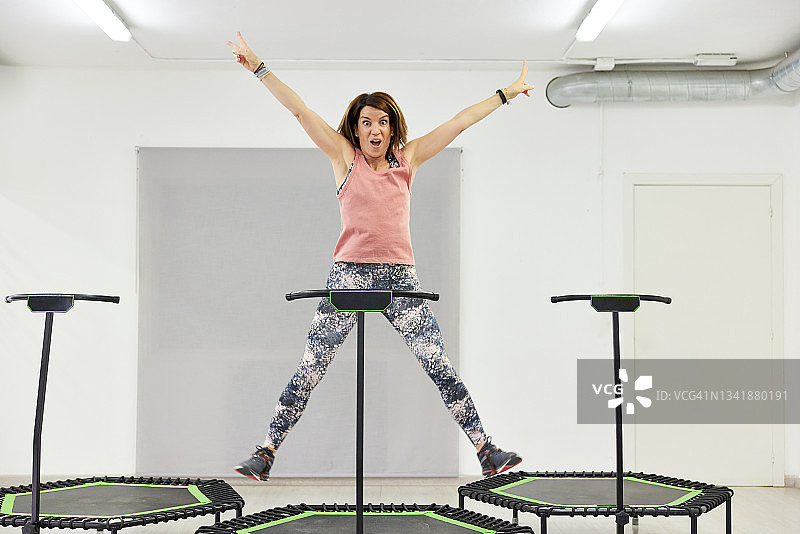 在健身蹦床上跳跃并举起双臂的女人图片素材