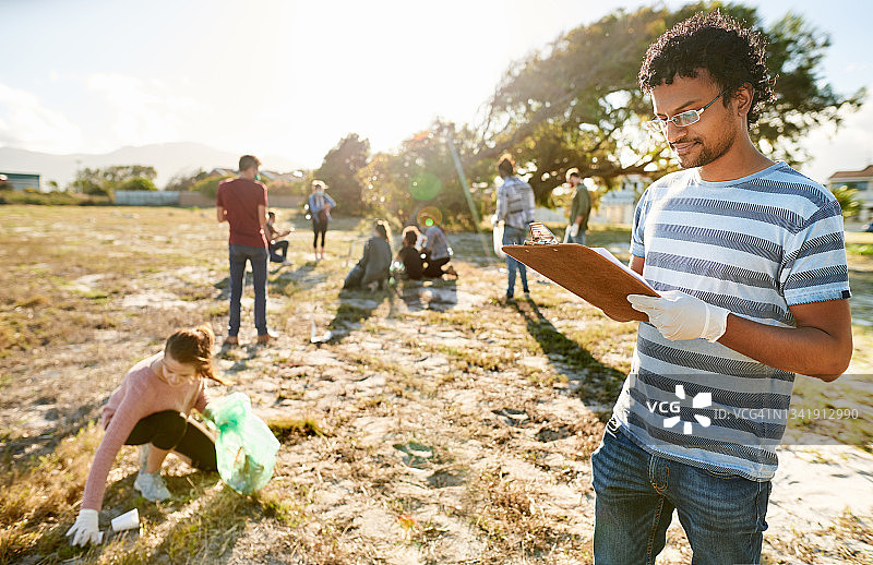 在社区清理期间，男志愿者拿着写字板站在田野里图片素材