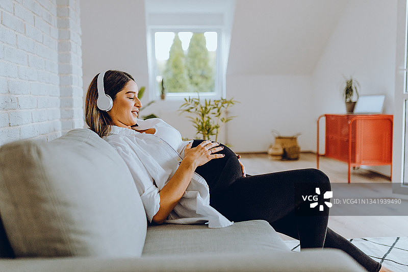 在家享受怀孕、使用笔记本电脑和听音乐的美丽女人图片素材