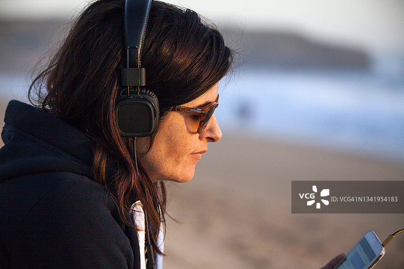 中年女人坐在海滩上听音乐图片素材