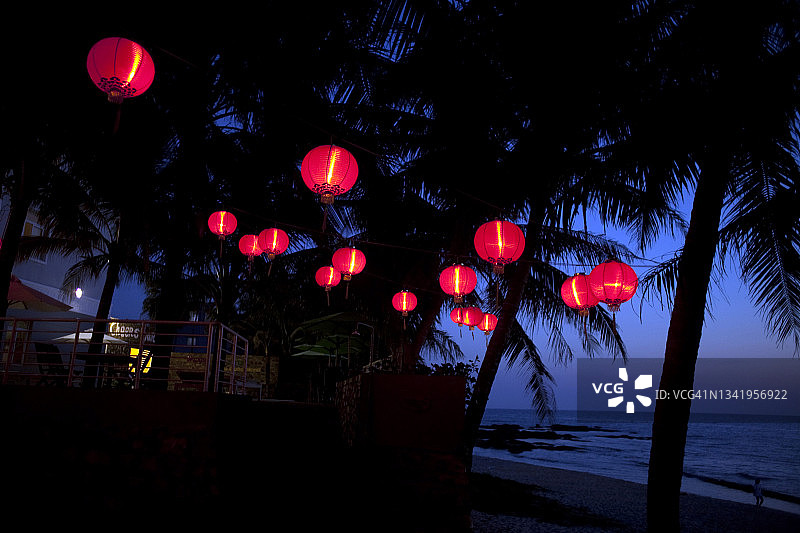 海滩附近棕榈树上悬挂的红色中式灯笼图片素材
