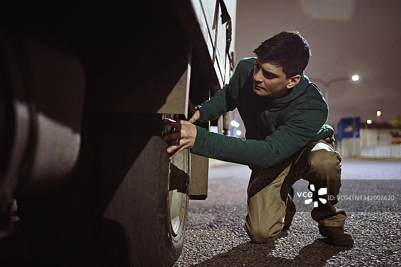 30岁左右的卡车司机在夜间检查后轮胎图片素材