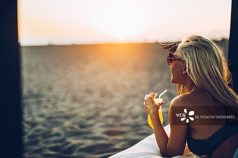 快乐的女人在日落时分的海滩上喝夏季鸡尾酒。图片素材