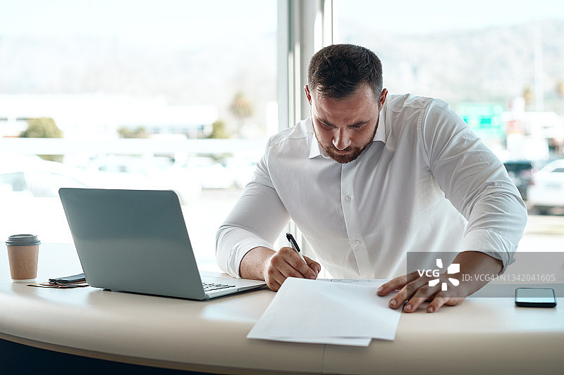 年轻汽车销售员在他的办公室里填写文件的照片图片素材