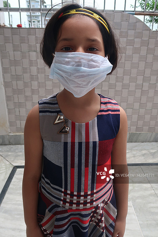 年轻印度女孩在室内戴着医用口罩，在全球突发卫生事件期间预防和防止冠状病毒 Covid-19 病毒传播图片素材