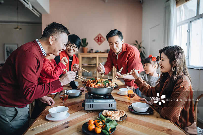 喜庆的亚洲家庭欢度中国新年，团圆饭享用美味的传统盆菜图片素材
