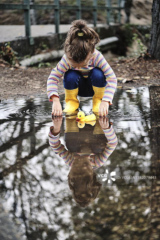 一个穿着黄色靴子的3岁女孩在水坑里玩橡皮鸭图片素材