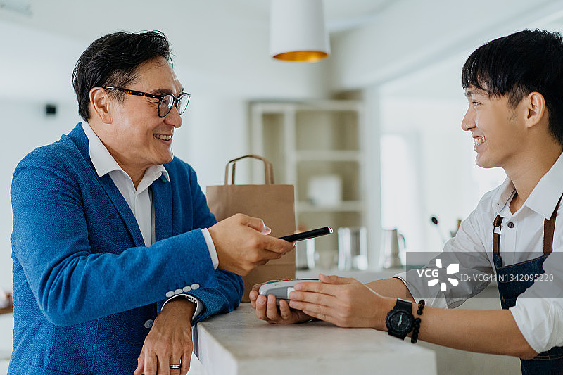 亚洲男人在咖啡馆使用手机App进行非接触式支付图片素材