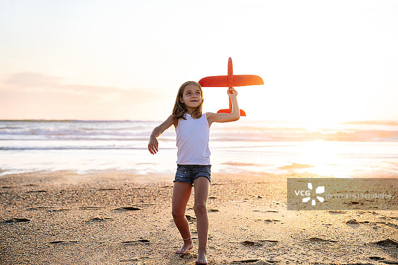 梦想飞行：女孩在夕阳下玩玩具飞机图片素材