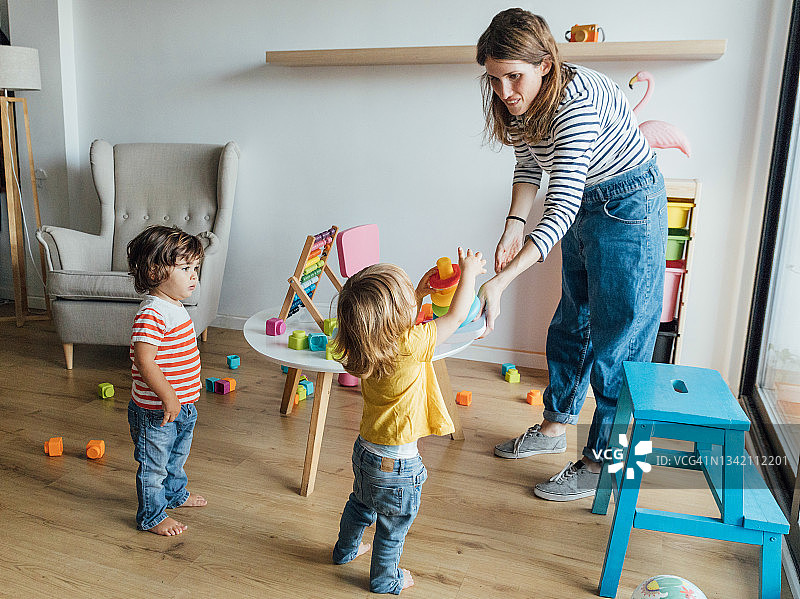 年轻女保姆在舒适的游戏室里和孩子们玩耍图片素材