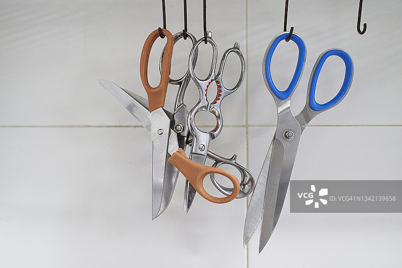 白色背景下挂在金属挂钩上的一套厨房剪刀的正面特写图片素材