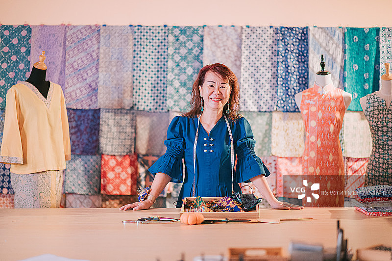 马来西亚华人中年妇女在她的蜡染旗袍面料零售店前微笑图片素材