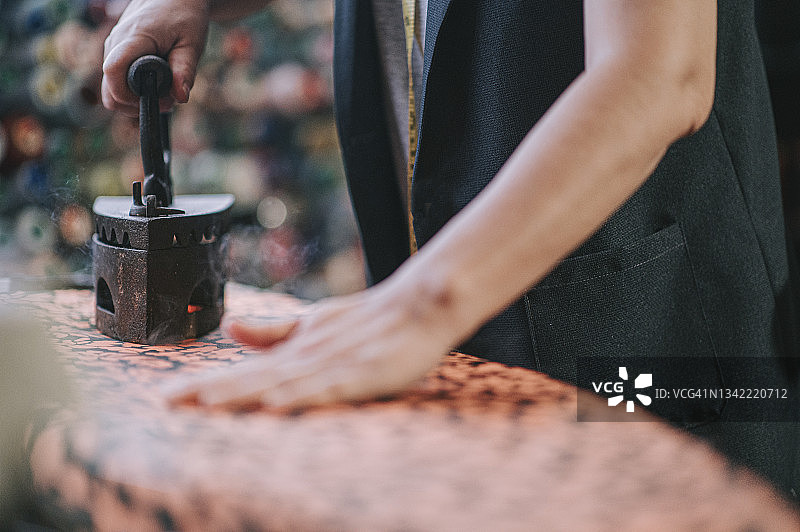 近距离拍摄亚洲华人妇女裁缝手用传统古玩铁器具在她的工作室熨布图片素材