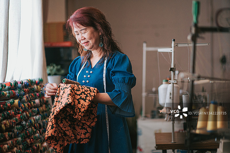 中国亚洲老年女裁缝在工作室选择与服装面料相配的线图片素材