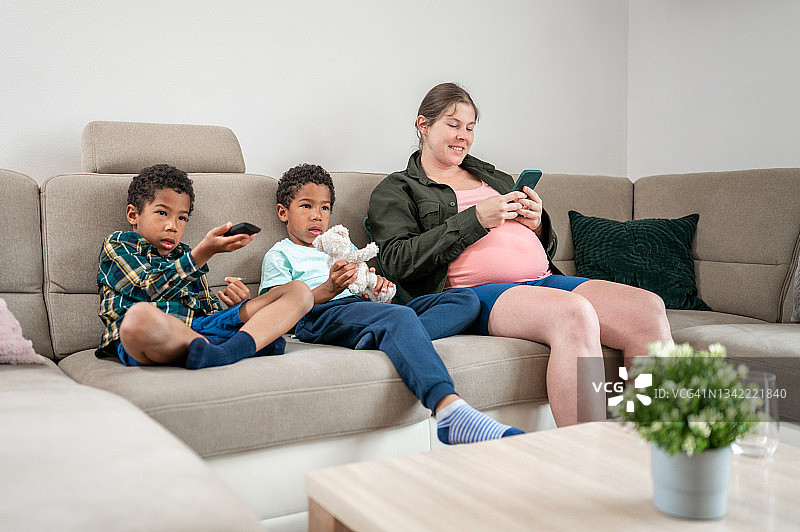 怀孕的成年女人和两个小男孩坐在客厅的沙发上图片素材