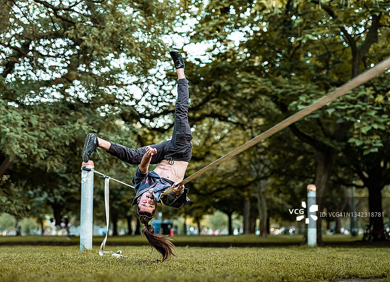年轻男子在公园的绳索上练习阿克罗瑜伽图片素材