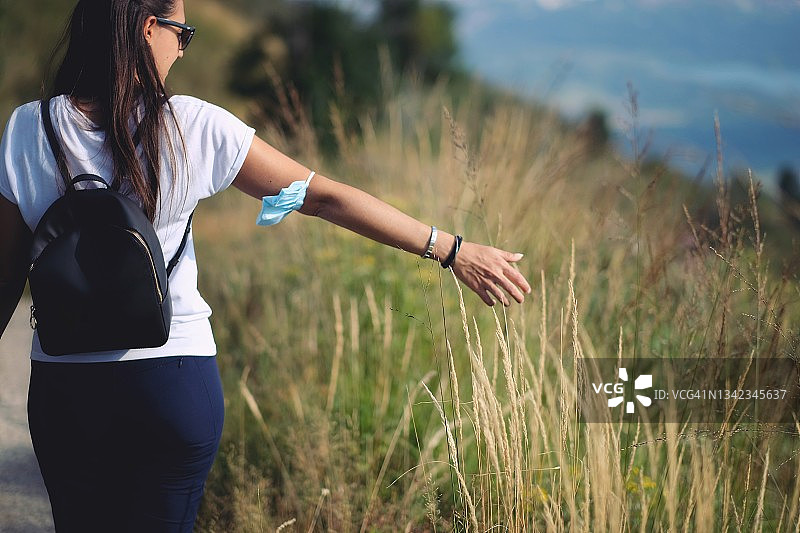 戴医用口罩的女孩手轻抚高草图片素材