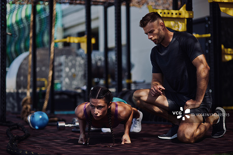 健身房里，健身女性在私人教练的指导下做俯卧撑图片素材