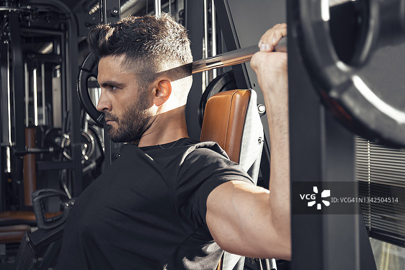 一个男人在健身房用史密斯机做肩部推举图片素材