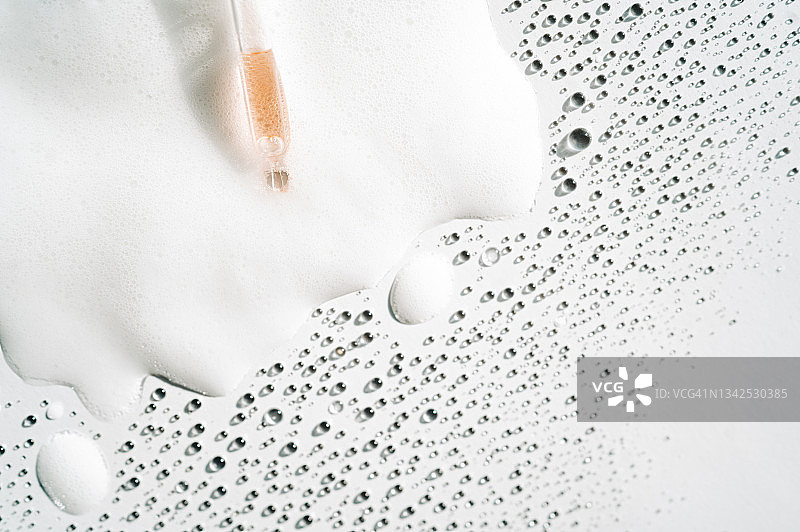 玻璃滴管滴在白色泡沫上的面部精华液，富含多种液滴。聚谷氨酸是一种新型透明质酸。设计文案的留白区域。扁平风格图片素材