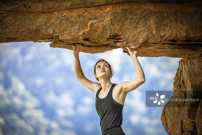女人在山上的岩石突出处向上看，攀岩图片素材