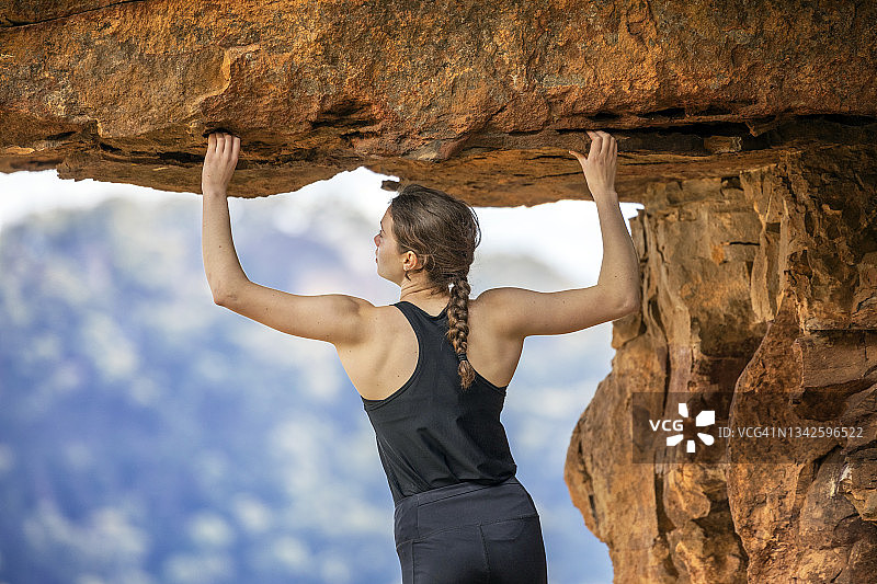 在岩石悬垂下，举起手臂抓住悬崖的攀岩女人图片素材
