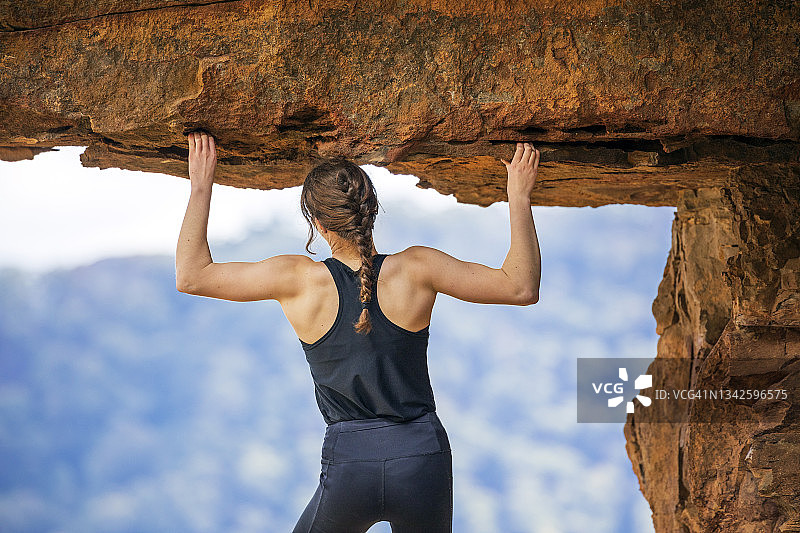 在岩石悬垂下，举起手臂抓住悬崖的攀岩女人图片素材