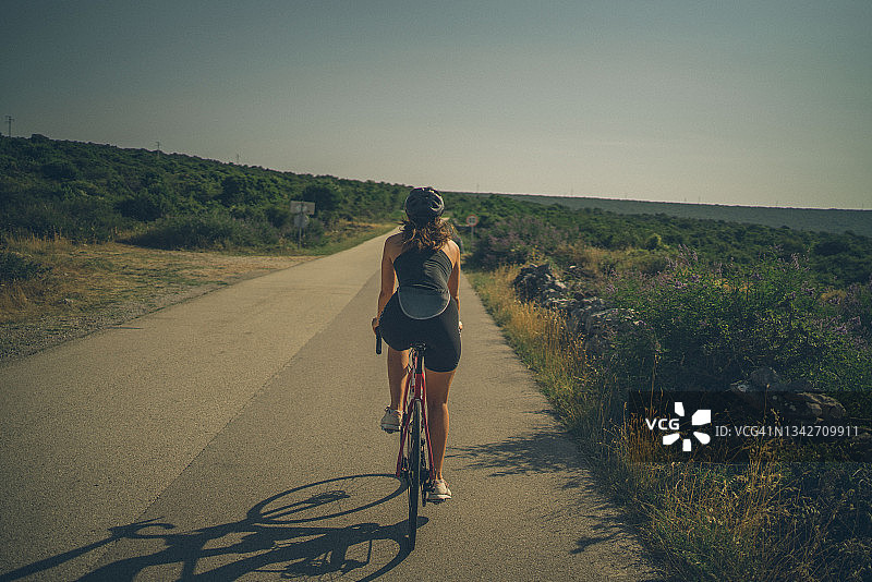女人在阳光明媚的乡村道路上骑公路自行车图片素材