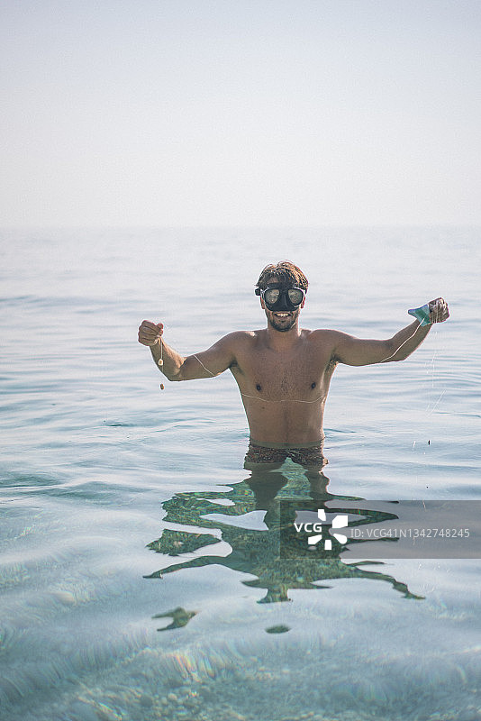 手举着刚捕获的鱼，面带微笑的年轻男子图片素材