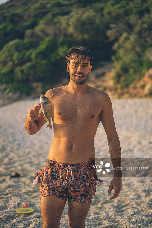 手举着刚捕获的鱼，面带微笑的年轻男子图片素材